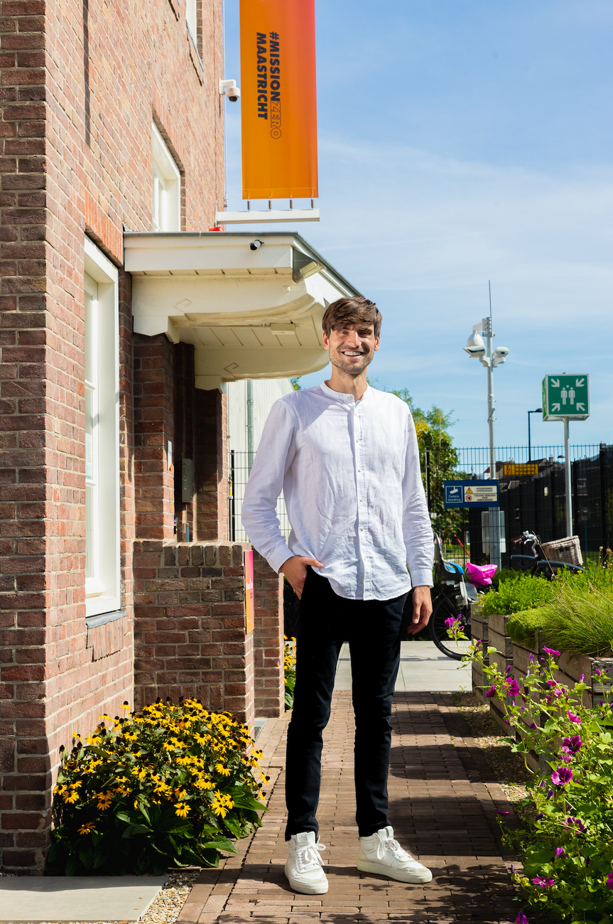een jongen met een wit hemd en zwarte broek die poseert voor een portiek
